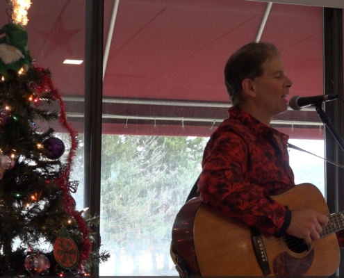 Dennis playing at holiday party for seniors with Christmas tree in background