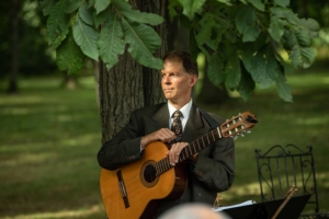 Dennis Winge with classical guitar standing under tree at wedding ceremony