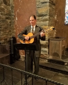 Dennis in suit playing classical guitar in a church for wedding ceremony