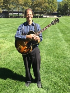 Dennis standing with guitar in park in Corning