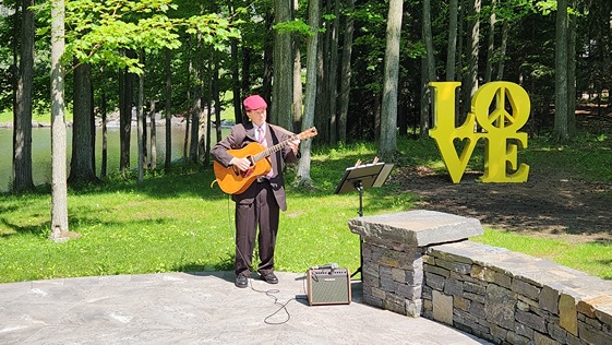Dennis Winge playing guitar at wedding ceremony with LOVE sign in background